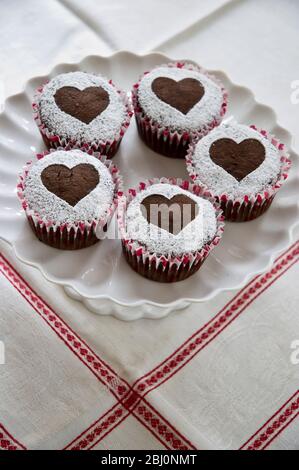 Fünf Schokoladen-Muffins mit Puderzucker in Herzform auf weißem Kuchenständer verziert - Stockfoto