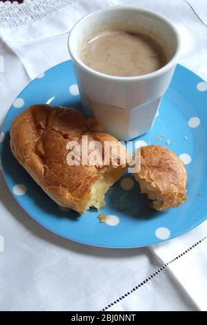 Weißer Becher Kaffee in blau gepunkteter Platte mit Croissant auf weißem Leinentuch mit Spitzenrand. Vintage-Stil - Stockfoto