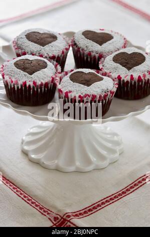 Fünf Schokoladen-Muffins mit Puderzucker in Herzform auf weißem Kuchenständer verziert - Stockfoto