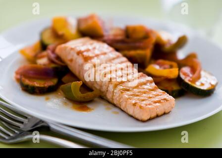 Kleines Stück Lachsfilet gegrillt, serviert auf Ratatouille. Eine einzige Portion auf weißem Teller. Kurze Schärfentiefe. - Stockfoto