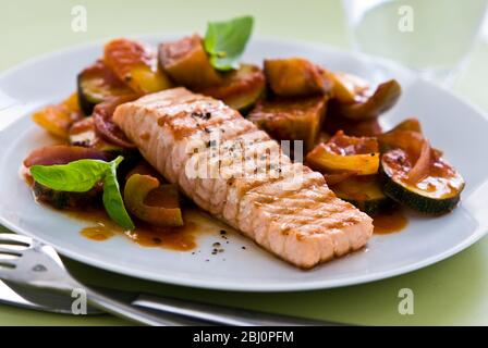 Kleines Stück Lachsfilet gegrillt, serviert auf Ratatouille. Eine einzige Portion auf weißem Teller. Schärfere Version. - Stockfoto