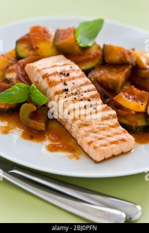 Kleines Stück Lachsfilet gegrillt, serviert auf Ratatouille. Eine einzige Portion auf weißem Teller. - Stockfoto