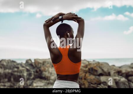 Rückansicht der afrikanischen Frau beim Fitnesstraining. Frau in Fitness tragen Stretching-Übungen mit den Armen über dem Kopf am Strand angehoben. Stockfoto