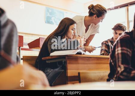 Lehrerinnen, die den Schülern während der Vorlesung im Klassenzimmer helfen. Professorin, die Studenten während einer Klasse an der High School hilft. Stockfoto