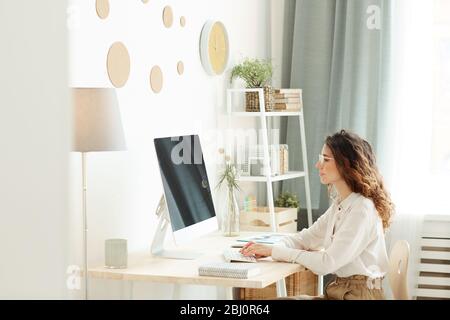 Junge Erwachsene Geschäftsfrau arbeitet an modernen Computer während zu Hause, horizontale Seitenansicht Aufnahme Stockfoto