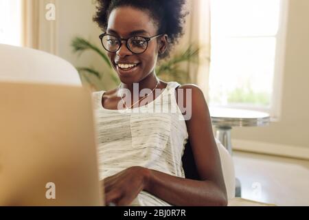 Glückliche Frau, die auf dem Sofa relaxt und am Laptop arbeitet. Afrikanische Frau mit Laptop und lächelnd am Wochenende. Stockfoto