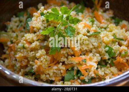 Gesunde Mittagszeit Salat aus Burghulweizen mit geriebener Karotte, Zitronensaft, Olivenöl, gehackte Gurke und Petersilie. - Stockfoto