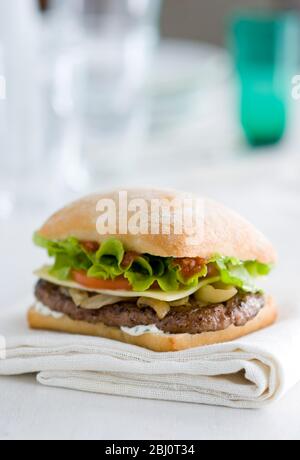 Gournet Cheeseburger mit Salat und Tomaten auf Ciabatta Brötchen auf weißer Serviette - Stockfoto