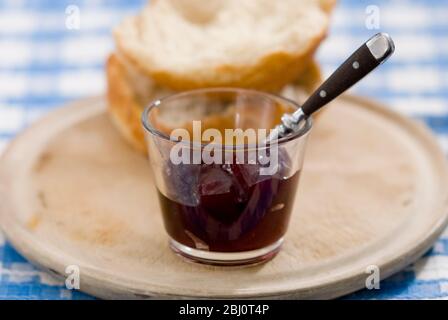 Kleine Glasschüssel aus kernloser Himbeermarmelade mit knusprigem Brot auf altem Schrubbelbrett - Stockfoto