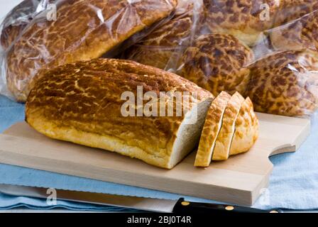 Tigerbrot wird auf Holzbrett geschnitten und mehr verpacktes Brot dahinter - Stockfoto