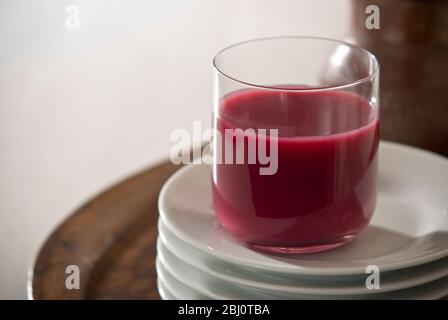 Granatapfelsaft in klarem Glas auf einem Stapel weißer Teller - Stockfoto