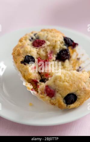 Frischer Beerenmuffin mit Himbeeren und Heidelbeeren, aufgerissen auf weißem Teller auf rosa Tuch - Stockfoto