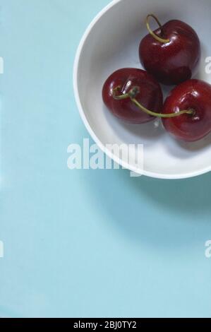 Drei rote Kirschen in kleiner weißer porzellaschale - Stockfoto