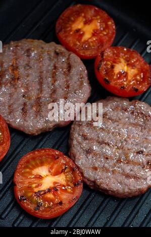 Beefburgers und halbierte Tomaten auf Antihaft-Grillpfanne gegrillt - Stockfoto