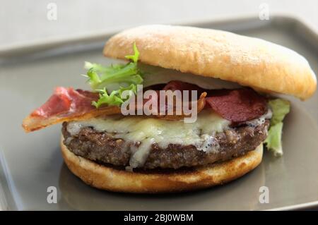 Hamburger vom Grill im Brötchen mit Frisee-Salat, gebratenem Speck und geschmolzenem Käse - Stockfoto