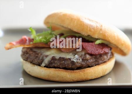 Hamburger vom Grill im Brötchen mit Frisee-Salat, gebratenem Speck und geschmolzenem Käse - Stockfoto