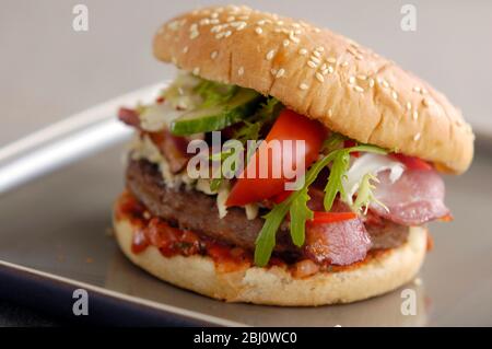 Hamburger vom Grill im Brötchen mit Frisee-Salat, Tomatensalsa, Tomatenkeil und gegrilltem Speckraspel und saurer Sahne - Stockfoto