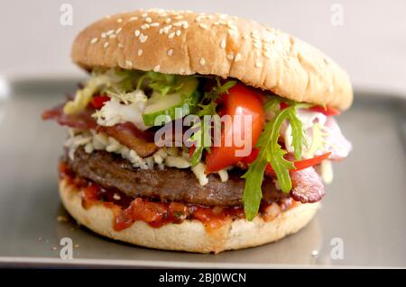 Hamburger vom Grill im Brötchen mit Frisee-Salat, Tomatensalsa, Tomatenkeil und gegrilltem Speckraspel und saurer Sahne - Stockfoto