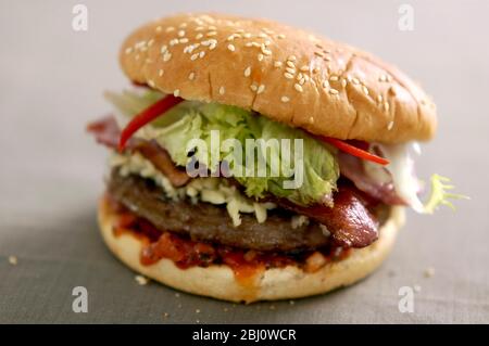Hamburger vom Grill im Brötchen mit Frisee-Salat, Tomatensalsa und Käse, Speck und Pfefferstreifen - - Stockfoto