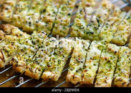 Frisch gebackene Käseherme, die auf dem Gestell gekühlt werden, mit geriebener Zucchini und geriebenem emmentaler auf Blätterteigblech gestreut und mit Hanfsamen bestreut Stockfoto