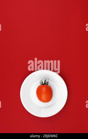 Kirschtomate auf weißem Teller auf rotem Hintergrund platziert Stockfoto