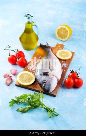 Frisch gefangener und gereinigter Brassen, fertig zum Kochen mit Tomaten, Knoblauch, Öl und Petersilie Stockfoto