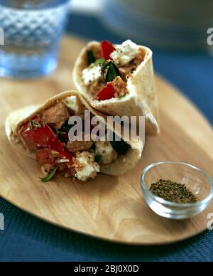 Pitta Brot in Taschen geschnitten gefüllt mit Salat von Tomaten, Thunfisch und Feta auf Holzbrett mit kleinen Glas Schüssel mit zerkleinerten schwarzen Pfeffer - Stockfoto