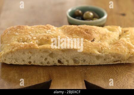 Olivenöl und Rosmarin Foccaccia Brot auf Holzbrett mit kleinen Schüsseln von einkerkerntem Olivenöl und ganze Oliven. - Stockfoto