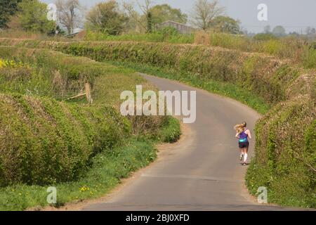 Eine junge Frau auf einer einsamen Landstraße, die während des Coronavirus-Ausbruchs läuft und sich ausübt. North Dorset England GB Stockfoto