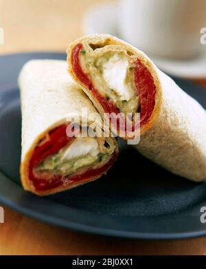 Wrap Sandwich in zwei geschnitten auf schwarzem Teller mit Tasse und Untertasse dahinter angeordnet - Stockfoto