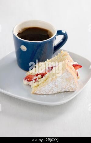 Stück Biskuitkuchen mit Puderzucker bestäubt und mit Erdbeeren und Sahne auf Teller mit kleinen blau-weiß gefleckten Becher schwarzen Kaffees gefüllt - Stockfoto