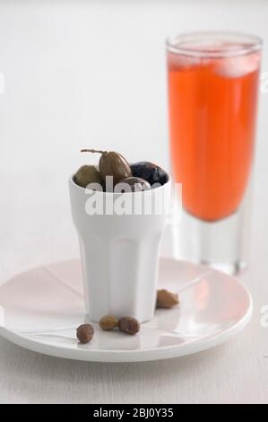 Ein Glas Campari und kleine weiße Keramiktopf mit italienischen Oliven - Stockfoto