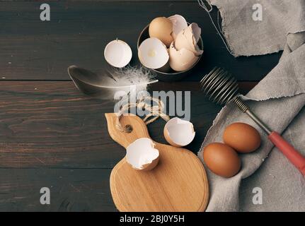 Braune rohe Hühnereier, Muscheln, Schneidebrett und Handbesen für Protein auf einem Holztisch, Draufsicht Stockfoto