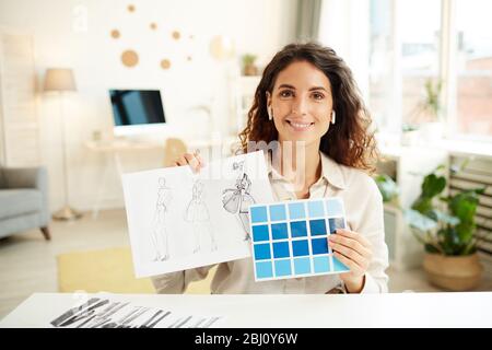 Weibliche Kleidung Designerin zeigt Skizzen und blaue Farbpalette auf der Kamera, horizontal Medium Porträt Stockfoto
