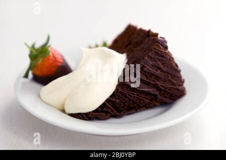 Scheibe von reichen dunklen Schokoladenkuchen mit Klecks Sahne und Erdbeere in Schokolade getaucht - Stockfoto