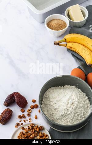 Rohzutaten auf weißem Marmorgrund für ein Rezept aus Haselnuss und Datteln aus Bananenbrot Stockfoto