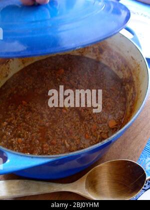 Den Deckel auf eine klassische italienische Bolognese Fleischsoße in großer blauer Emailkasserole mit großem Holzlöffel aufrichten - Stockfoto