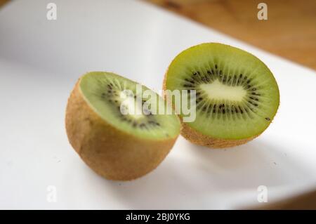 Kiwi-Frucht halbiert, um innere Textur und Struktur auf weißer Keramikoberfläche5 - Stockfoto