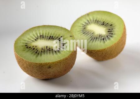 Kiwi-Frucht halbiert, um innere Textur und Struktur auf weißer Keramik-Oberfläche zu zeigen - Stockfoto