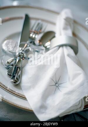 Festliche Tischkulisse in Weiß und Silber mit bestickter Serviette, Bändern und Süßigkeiten - Stockfoto