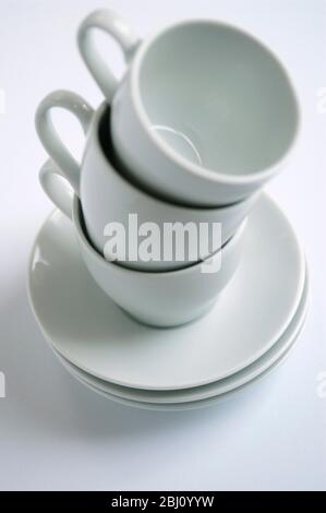 Drei weiße Kaffeetassen und Untertassen auf weißer Oberfläche gestapelt - Stockfoto