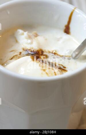 Eistkaffee mit Vanilleeis und Schokoladensirup in weißem Becher auf kariertem Liinen-Tuch - Stockfoto