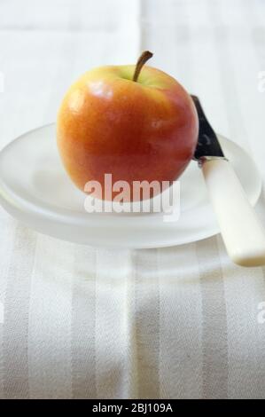 Ein Apfel auf einer geschliffenen Glasplatte mit Messer - Stockfoto