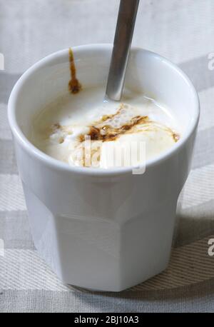 Eistkaffee mit Vanilleeis und Schokoladensirup in weißem Becher auf kariertem Liinen-Tuch - Stockfoto