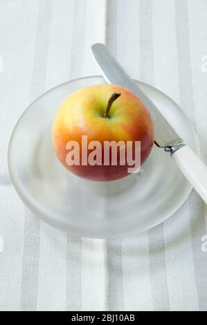 Ein Apfel auf einer geschliffenen Glasplatte mit Messer - Stockfoto