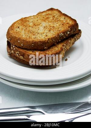 Drei Scheiben brauner Vollkorntoast auf einem Stapel weißer Teller mit Besteck - Stockfoto