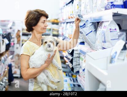 Vorsichtig fröhlich positive ältere Frau, die Tierhandlung auf der Suche nach Trockenfutter für ihren Hund besucht Stockfoto