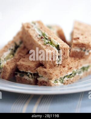 Kleine Sandwiches aus braunem Brot, in Finger geschnitten mit Frischkäse, Gurke, Kresse und getrockneten Tomaten - Stockfoto