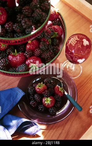 Erdbeeren und Brombeeren auf hohem Ständer mit Weinglas und Teller - Stockfoto
