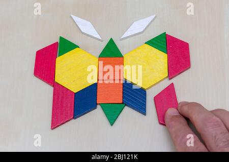 Tangram Schmetterling farbigen Kind geometrischen Puzzleteil mit Hand Füllung in das letzte Stück auf braunem Hintergrund. Stockfoto